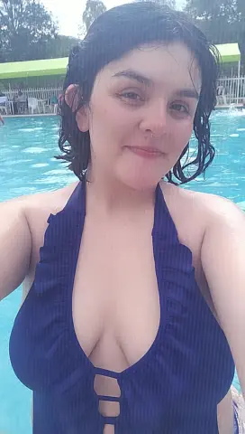 Smiling woman in a navy blue ruffled halter swimsuit relaxing by a bright blue swimming pool.