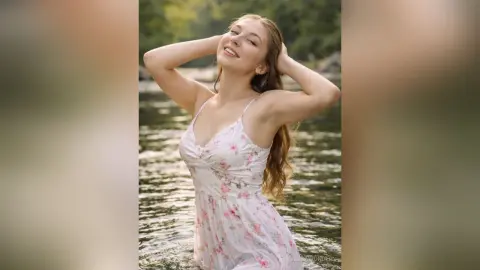 Smiling young woman in a white floral sundress relaxing by a serene forest river in natural sunlight.