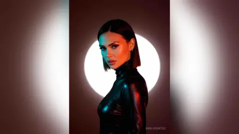 Elegant woman in a black leather turtleneck posing against a dramatic circular light backdrop.