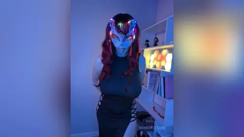 Woman in a black outfit wearing a glowing LED kitsune mask in a room with warm hexagonal lights.