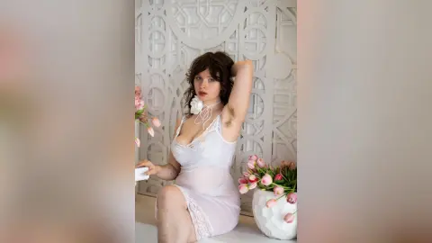 Curvy woman in a white lace slip dress sitting by pink tulips in a bright, minimalist room.