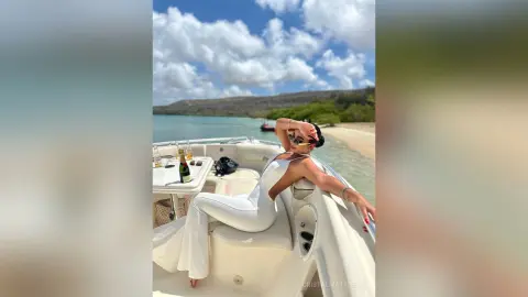 CristalMatthews reclines on a white boat deck wearing a white sleeveless bodysuit or swimsuit under a bright blue sky.