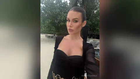 Elegant woman in a black chic outfit posing outdoors in a tropical garden setting.