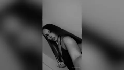 Black and white portrait of a woman in a black tank top posing against a minimalist wall background.