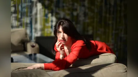 ViolaWin — ViolaWin lies on a tan sofa wearing a red long-sleeved top and looking at the camera.