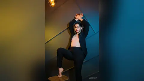 JessieLiu poses with one leg raised on a block, wearing an open black shirt and black trousers.