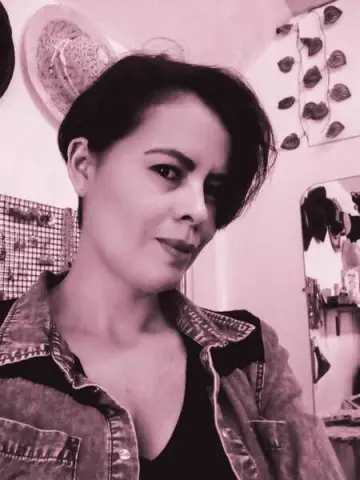 Woman in a denim shirt and black top posing in a bright indoor room with a soft pink aesthetic.
