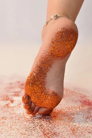 Close-up of a person's foot covered in sparkling orange glitter on a white surface, creating a festive mood.