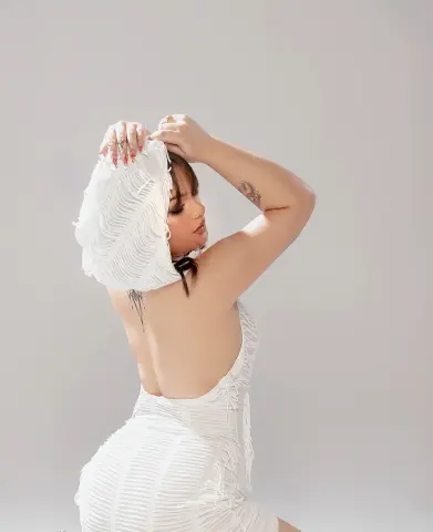 Woman in a white textured backless dress posing against a plain background in a minimalist aesthetic.