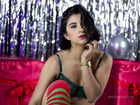 Young woman in green lace lingerie posing against silver tinsel and pink gift boxes for a festive celebration.
