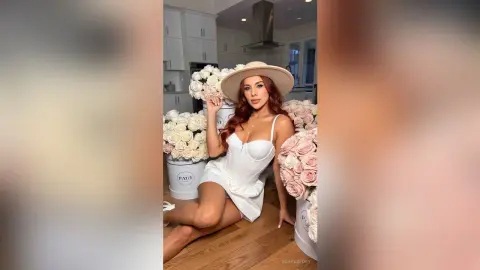 Elegant woman in a white dress and wide-brimmed hat posing with large bouquets of pink and white roses.