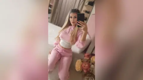Young woman in pink loungewear taking a selfie in a bright bedroom setting.