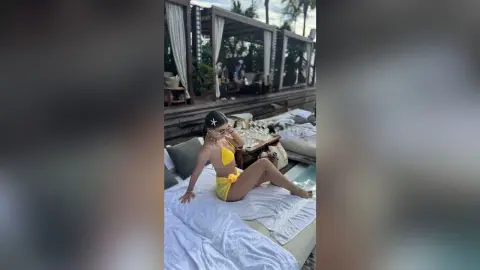 Young woman in a yellow bikini relaxing on a white lounge bed at a tropical outdoor resort patio.