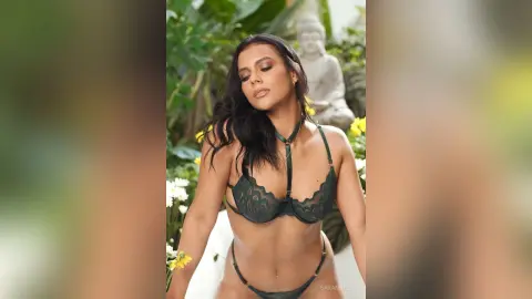 Beautiful woman in dark green lace lingerie posing in a lush tropical garden setting.
