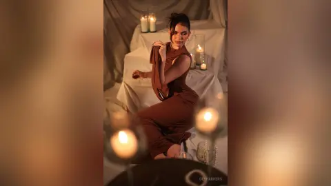 Elegant woman in a brown sleeveless dress sitting in a romantic candlelit room with a dreamy mood.