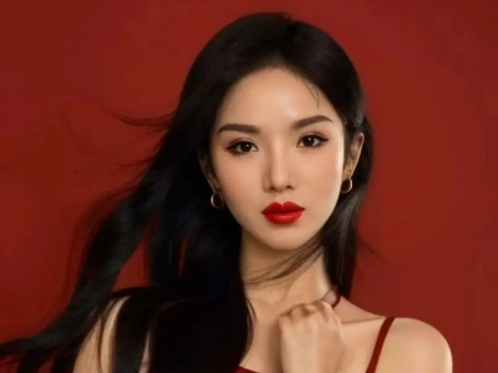 Elegant woman with long dark hair and red lipstick posing against a bold red background.