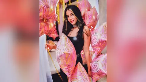 JessieLiu poses in a black leather bodysuit surrounded by pink and gold swirl-patterned balloons.