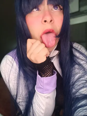 Cosplayer with long blue hair and white shirt making a playful expression in a close-up portrait.