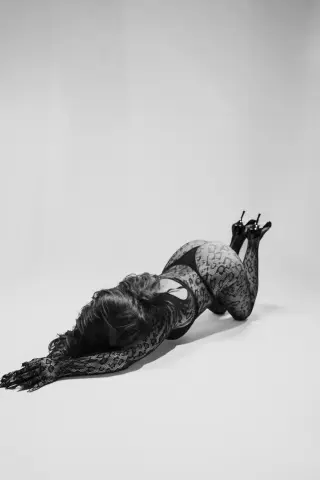Elegant woman in a black lace bodysuit posing on a white studio floor in a moody black and white portrait.