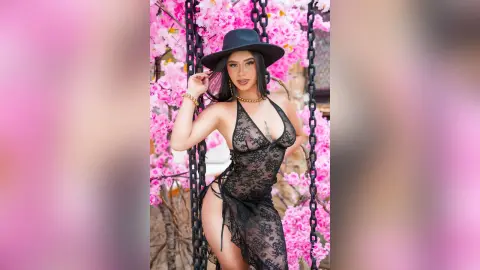 Glamorous woman in a black lace dress and wide-brimmed hat posing amidst blooming pink cherry blossoms.