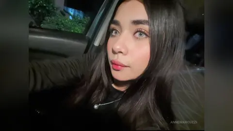 Young woman with long dark hair wearing a black top sitting in a car at night with soft lighting.