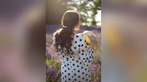 Woman in white polka dot dress standing in a dreamy lavender field at sunset.