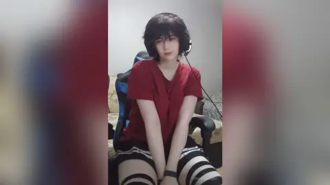 Young woman with headphones wearing a red t-shirt and striped skirt sitting in a gaming chair.
