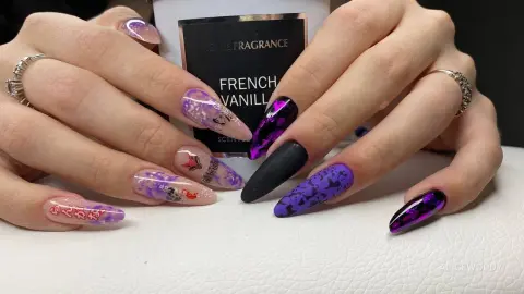 Close-up of hands with purple and black butterfly nail art holding a French Vanilla scented candle jar.
