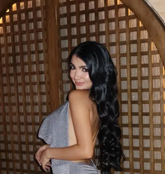 AllysonDiiamond poses with long dark hair, wearing a white lace top that shows deep cleavage and her bare shoulders.