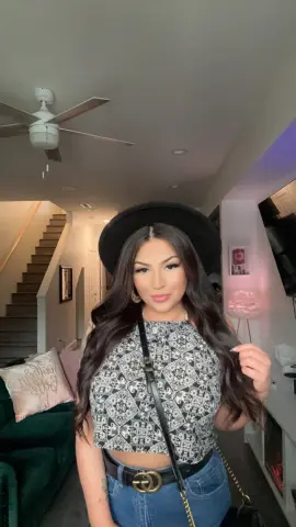 Ameliajade111 — Stylish woman in a patterned halter top and black wide-brim hat posing in a modern living room.