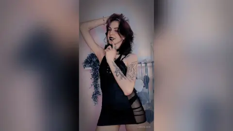 LorenLoiss poses with one hand near her mouth, wearing a black cut-out bodysuit and a black choker.