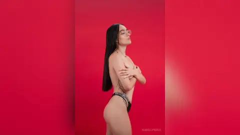 Young woman with long dark hair in black lingerie posing confidently against a vibrant red studio background.