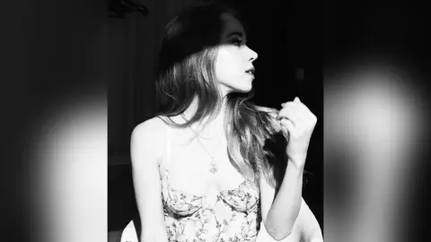 Moody black and white portrait of a woman in a floral lace camisole looking away in soft lighting.