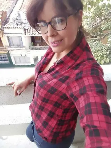 Smiling woman in a red plaid shirt relaxing on a sunny balcony outdoors.