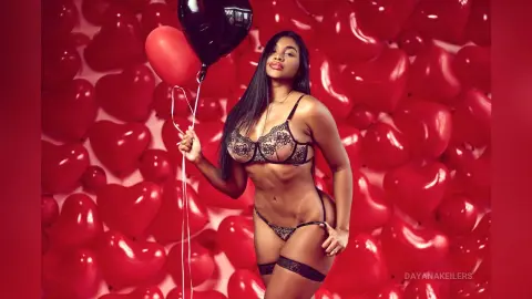 DayanaKeilers poses in black lace lingerie against a wall of red heart-shaped balloons.