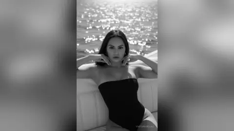 Elegant woman in a black strapless bodysuit relaxing on a yacht against a sparkling ocean background.