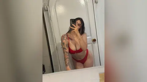 BonnieRider poses in a red bikini, showing off her tattoos and long dark hair in a mirror selfie.