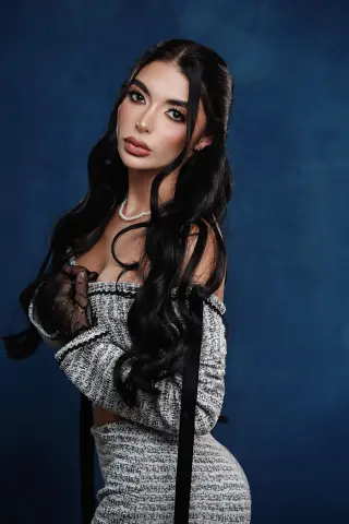 Elegant woman with long dark hair in a grey tweed outfit posing against a moody blue studio background.
