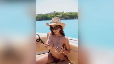 Brunette woman in a straw hat and bikini relaxing on a boat in turquoise tropical waters.