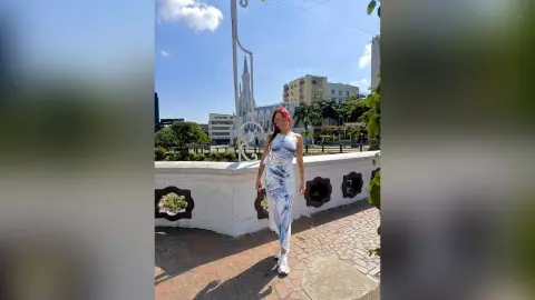 MilaGreco stands outdoors in a white and blue tie-dye dress, showing off her long hair and athletic build against a city background.