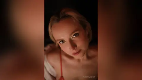 Close-up portrait of a blonde woman with a soft, moody expression in warm, dim lighting.