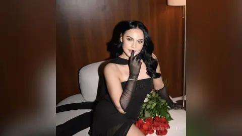 Elegant woman in a black evening gown and sheer gloves sitting on a white sofa in a moody indoor setting.