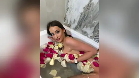 Young woman relaxing in a luxury marble bathroom bathtub filled with red rose petals for a romantic spa mood.