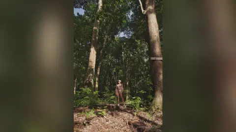 LaurentBelluci stands in a sunlit forest wearing a patterned one-piece swimsuit or bodysuit.