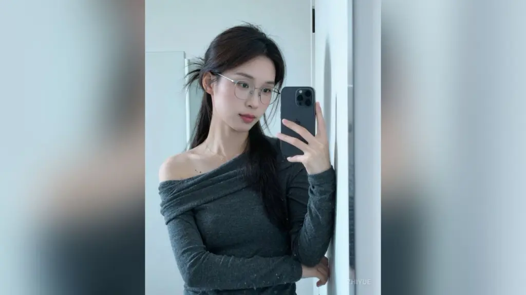 ZhiYue poses outdoors in a grey off-the-shoulder top with her long brown hair tied with a blue ribbon.
