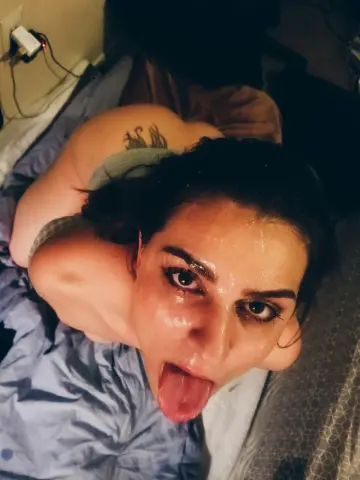 Sweaty woman in a grey tank top lying on a bed with a playful expression.