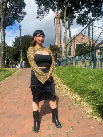 Young woman in a leopard print shrug and black skirt standing on a brick path near a park tower.
