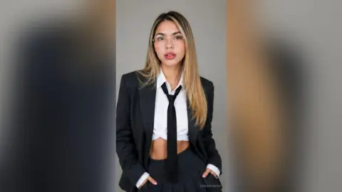 Confident young woman in a black professional suit and white shirt posing against a neutral studio background.