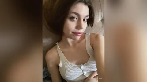 Young woman in a white ribbed tank top relaxing on a couch with a peaceful expression.