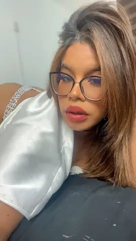 Close-up portrait of a woman with brown hair and glasses wearing a white satin top in a soft indoor setting.